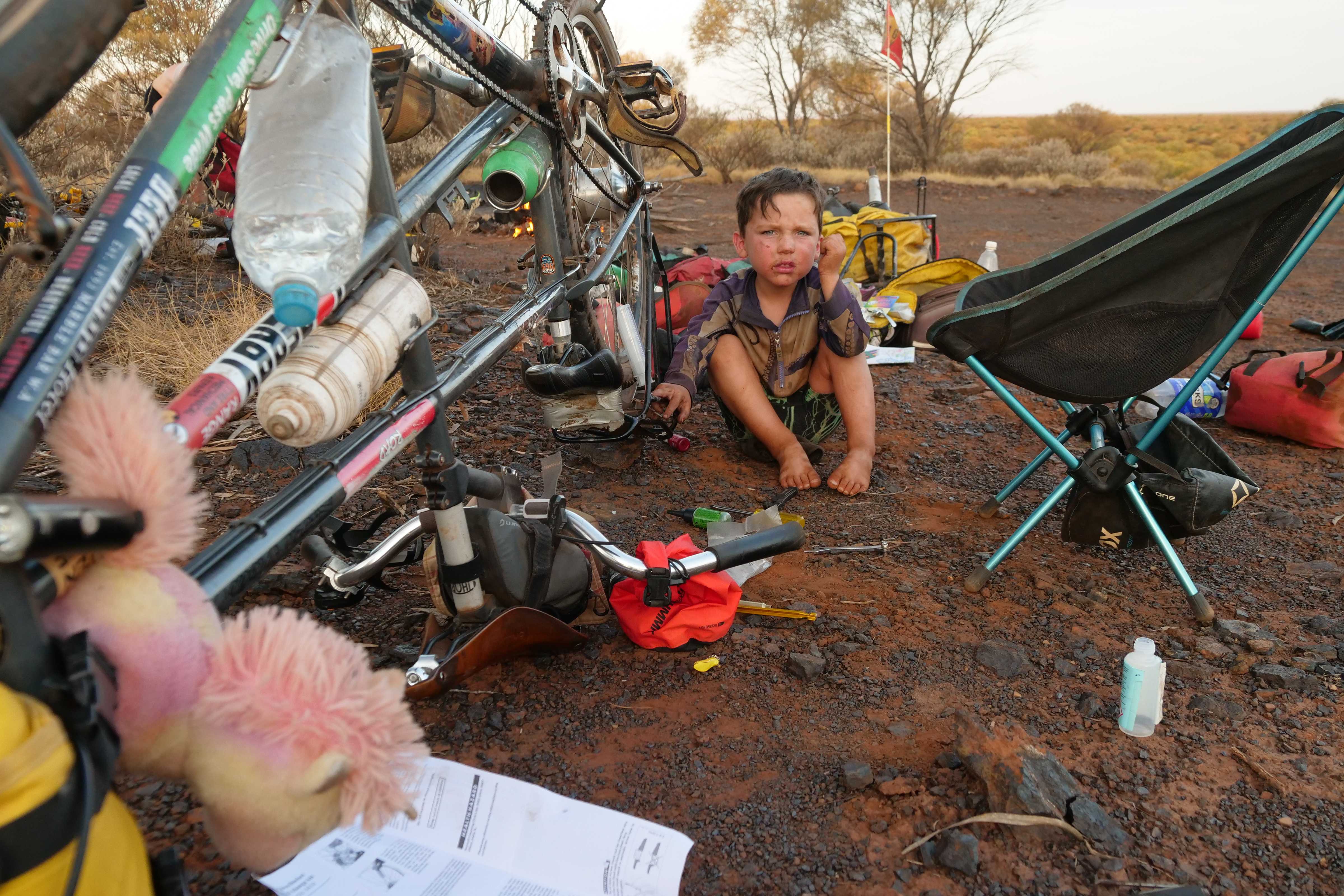 Wilfy at an outback Australian campsite with bike upside down for cleaning and tyre repair.