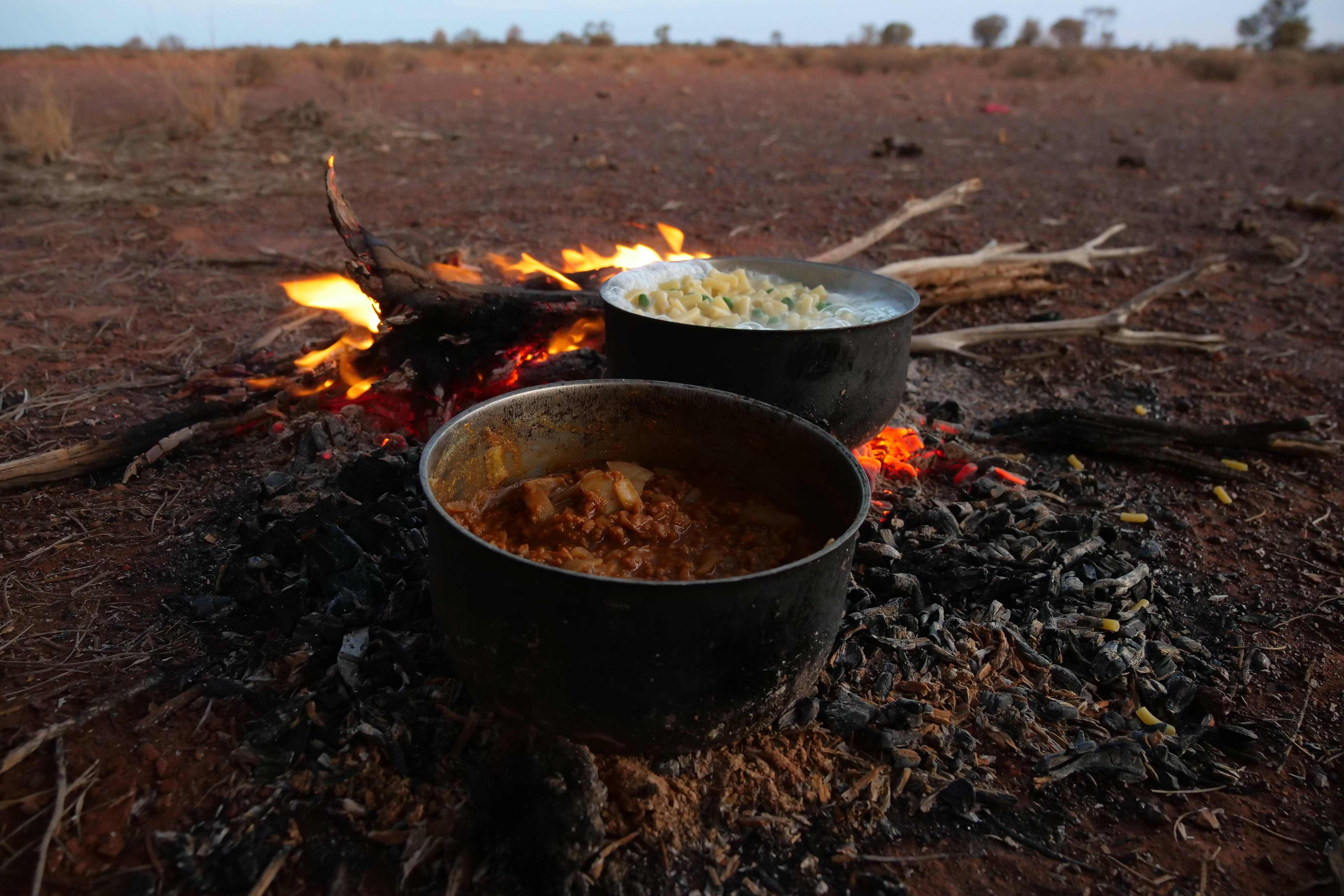 Cooking pots sitting on open fire in flat desert country. 